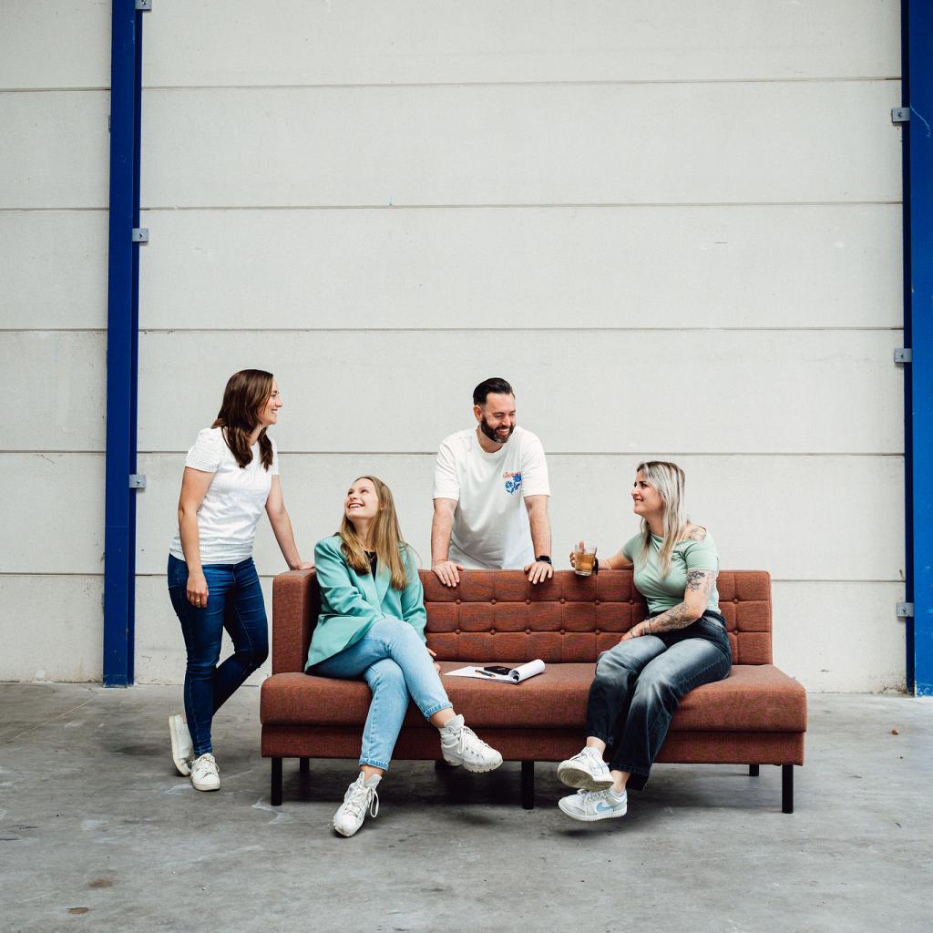 4 personen op een bank in een lege hal in interactie met elkaar.