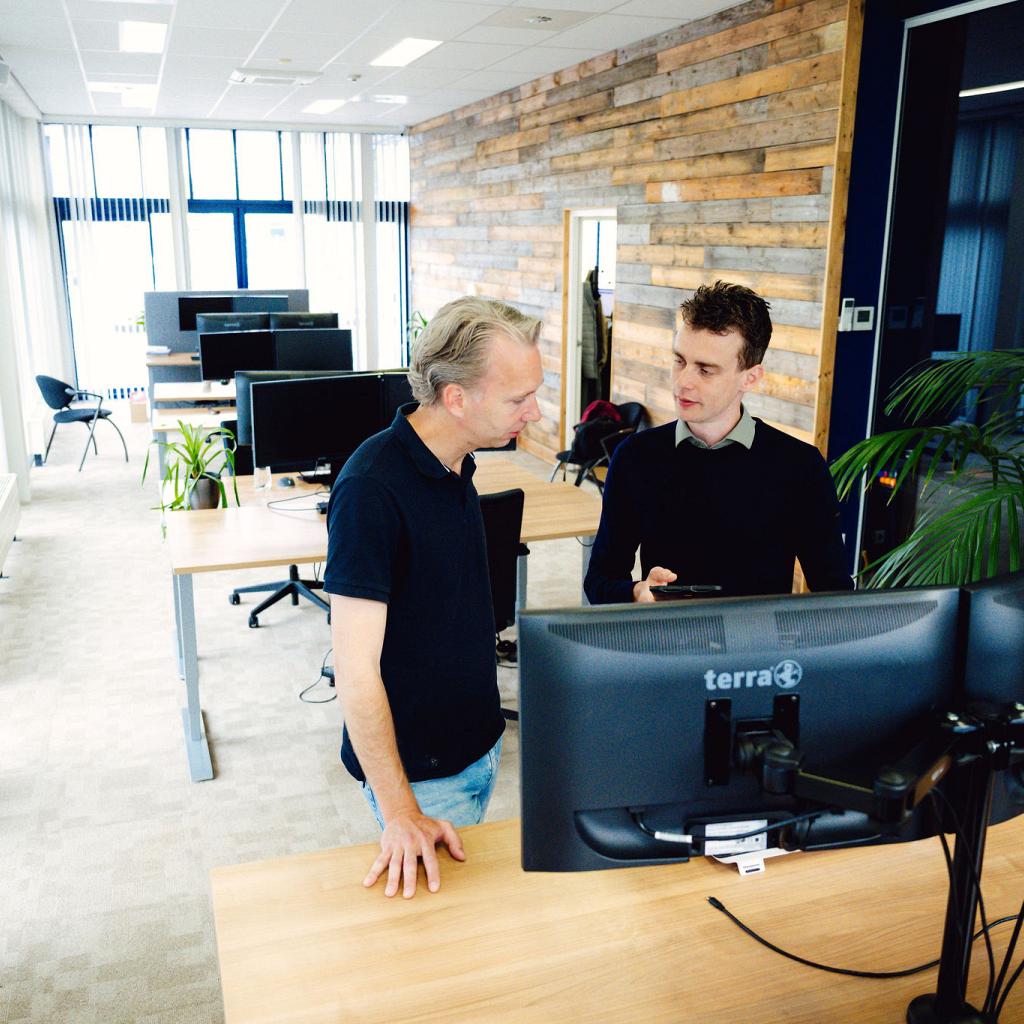 2 mannen staand achter een bureau in een leeg kantoor, in interactie.