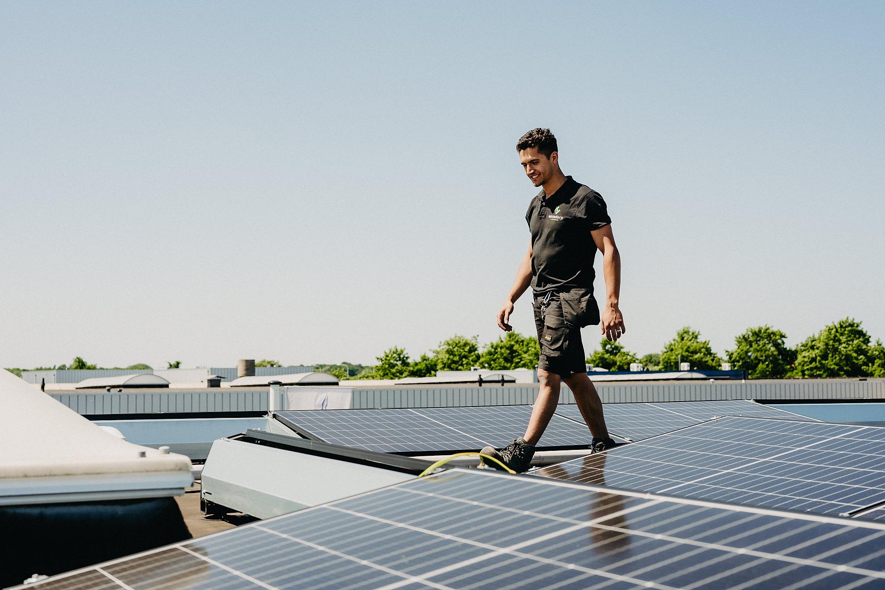 Man in zwarte kleding loopt op een dak tussen zonnepanelen door. 